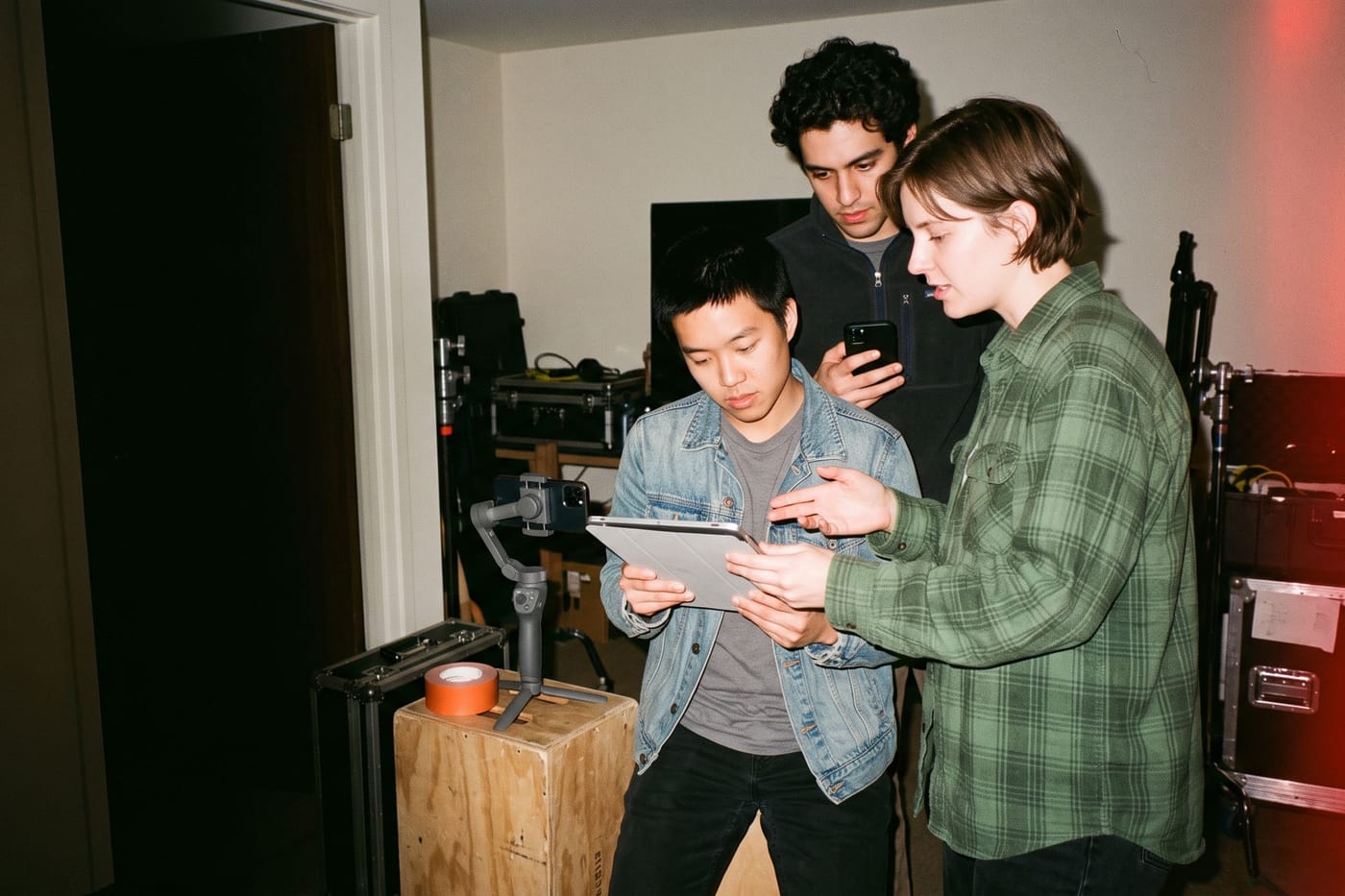 Three filmmakers standing around a tablet in a gear room, reading a scene together